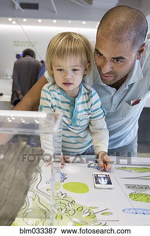 Stock Photo - Hispanic father and son using cell phone in museum. Fotosearch