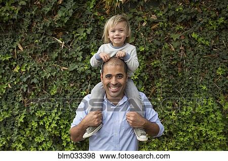 Hispanic father carrying son on shoulders near ivy wall View Large Photo Image Stock Photo - Hispanic father carrying son on shoulders near ivy wall. Fotosearch
