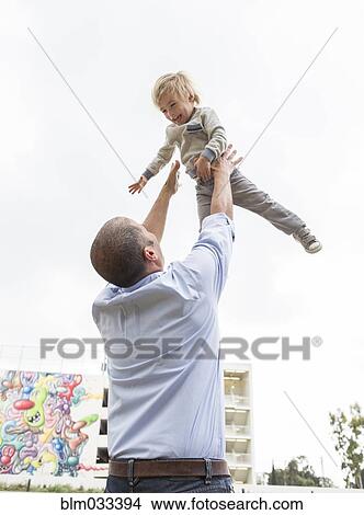 Picture - Hispanic father throwing son in air outdoors. Fotosearch