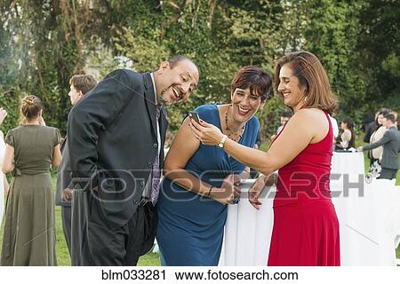 Stock Image - Hispanic friends using cell phone at wedding. Fotosearch