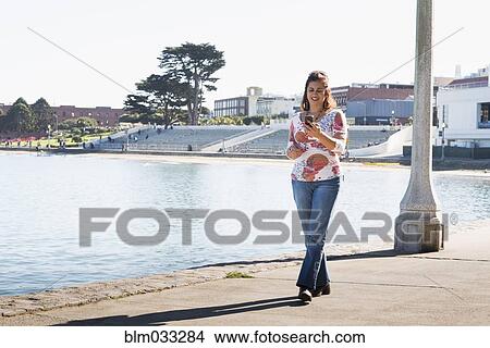 Picture - Hispanic woman texting on cell phone at waterfront. Fotosearch