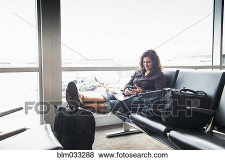 Stock Photo - Hispanic woman texting on cell phone in airport. Fotosearch