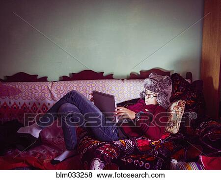 Stock Photo - Mixed race boy wearing fur hat using digital tablet on sofa. Fotosearch