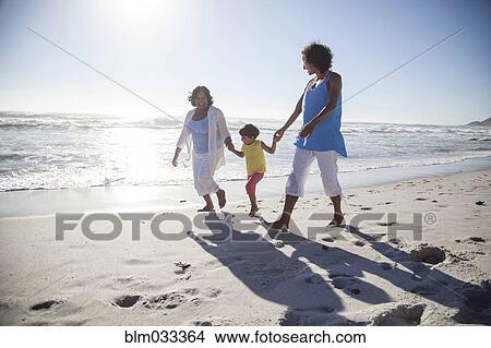 Picture - Mixed race grandmother, daughter and granddaughter walking on beach. Fotosearch