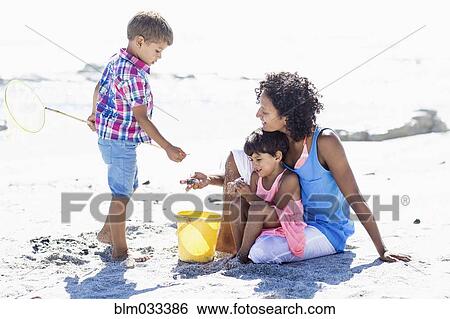 Stock Photograph - Mixed race mother and children playing on beach. Fotosearch