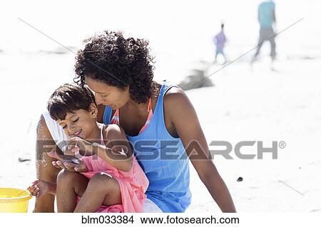Picture - Mixed race mother and daughter playing on beach. Fotosearch