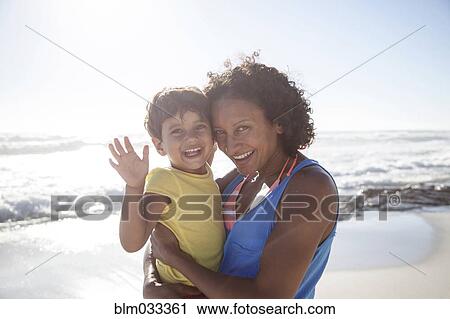 Stock Image - Mixed race mother and daughter waving on beach. Fotosearch