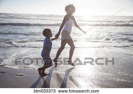 Stock Image - Mixed race mother and son playing in ocean waves on beach. Fotosearch
