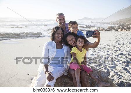 Stock Photograph - Mixed race multi-generation family taking cell phone selfie on beach. Fotosearch