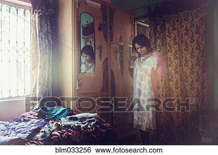 Stock Photograph - Mixed race woman examining dress in bedroom. Fotosearch