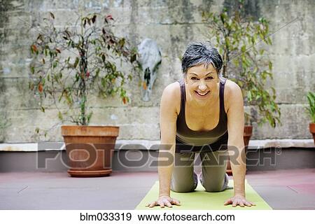 Stock Photo - Older Caucasian woman practicing yoga in courtyard. Fotosearch
