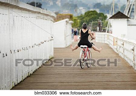 Stock Photograph - Older Caucasian woman riding bicycle on wooden dock. Fotosearch