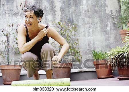 Stock Image - Older Caucasian woman rolling up yoga mat in courtyard. Fotosearch