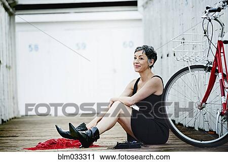 Stock Image - Older Caucasian woman sitting with bicycle on wooden dock. Fotosearch
