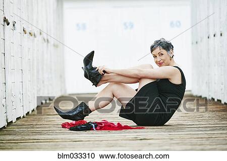 Stock Image - Older Caucasian woman taking off boots on wooden dock. Fotosearch
