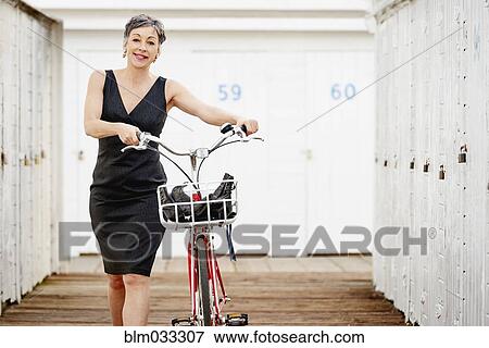 Stock Photo - Older Caucasian woman walking bicycle on wooden dock. Fotosearch
