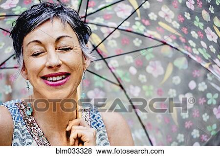 Stock Photo - Older Caucasian woman with eyes closed holding umbrella. Fotosearch