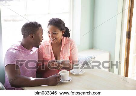 Stock Photograph - Smiling couple using cell phone at breakfast. Fotosearch