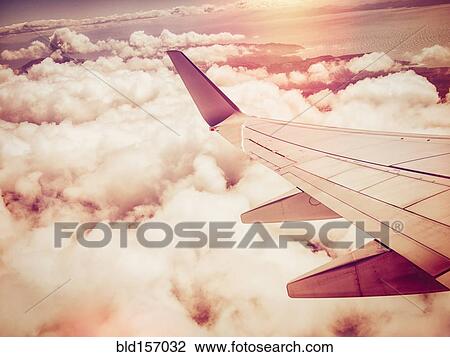 Stock Image - Aerial view of airplane wing flying over clouds in sky. Fotosearch