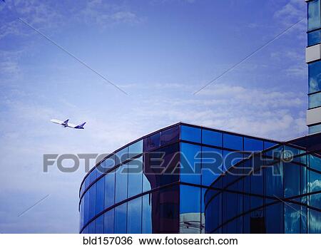 Stock Photograph - Airplane flying over airport tower. Fotosearch