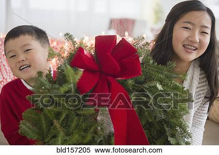 Stock Photography - Asian brother and sister carrying Christmas wreath. Fotosearch