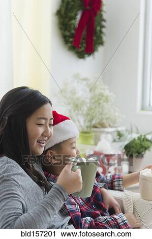 Stock Image - Asian brother and sister drinking hot cocoa at Christmas. Fotosearch
