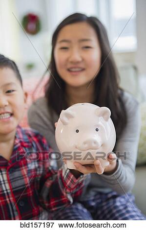 Asian brother and sister holding piggy bank in living room View Large Photo Image Stock Photo - Asian brother and sister holding piggy bank in living room. Fotosearch