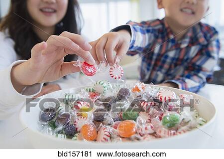 Stock Image - Asian brother and sister picking candy from bowl. Fotosearch