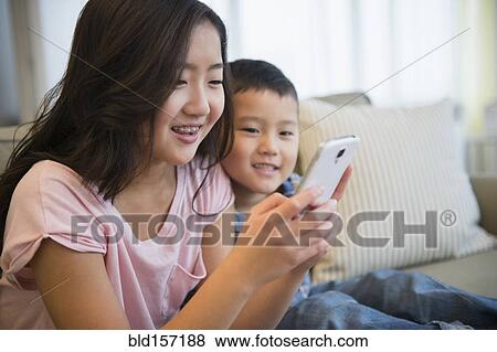 Stock Photo - Asian brother and sister using cell phone on sofa. Fotosearch