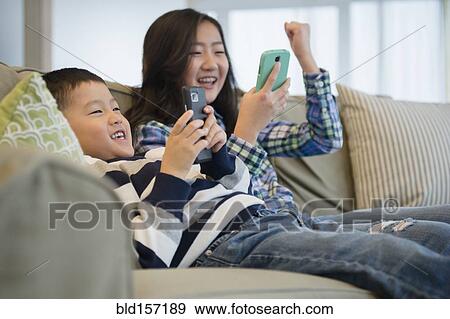 Stock Photo - Asian brother and sister using cell phones on sofa. Fotosearch