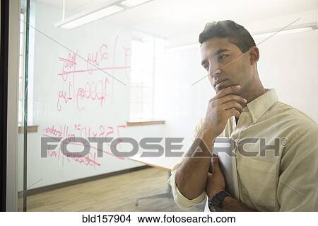 Picture - Asian businessman examining writing on glass window in office. Fotosearch