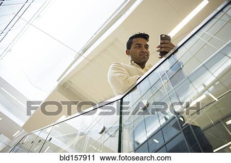 Stock Image - Asian businessman texting with cell phone on office staircase. Fotosearch