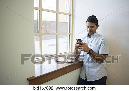 Stock Image - Asian businessman using cell phone and digital tablet at window. Fotosearch