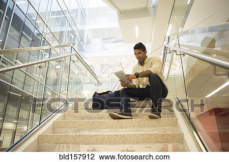 Stock Image - Asian businessman using digital tablet on office staircase. Fotosearch