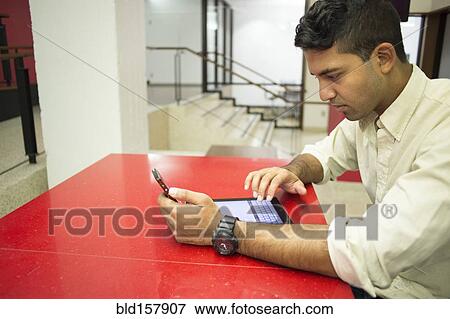 Stock Photo - Asian businessman using digital tablet and cell phone in office. Fotosearch