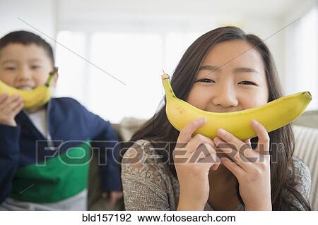 Stock Image - Asian children holding bananas in front of faces for smiles. Fotosearch