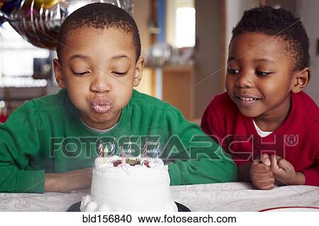 Stock Image - Black boy blowing out cake candles at party. Fotosearch