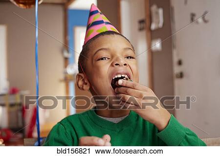 Stock Image - Black boy eating cake at party. Fotosearch