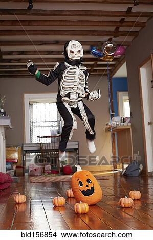 Picture - Black boy jumping over pumpkin in skeleton Halloween costume. Fotosearch