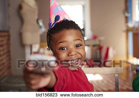 Stock Image - Black boy offering cupcake at party. Fotosearch