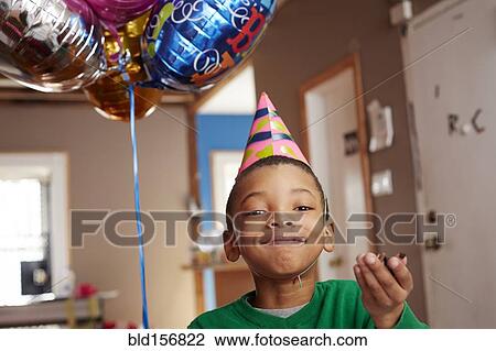 Stock Image - Black boy wearing party hat holding balloons. Fotosearch