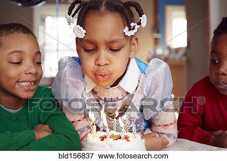 Stock Photo - Black girl blowing out cake candles at party. Fotosearch
