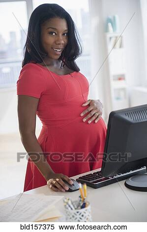 Stock Photography - Black pregnant businesswoman working at computer in office. Fotosearch