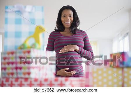 Stock Image - Black pregnant woman admiring gifts at baby shower. Fotosearch