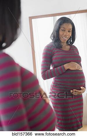 Stock Photograph - Black pregnant woman admiring her stomach in mirror. Fotosearch