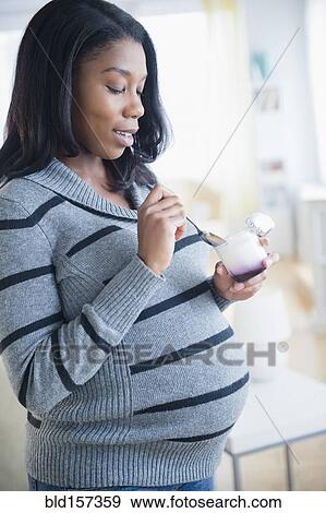Stock Photo - Black pregnant woman eating yogurt. Fotosearch