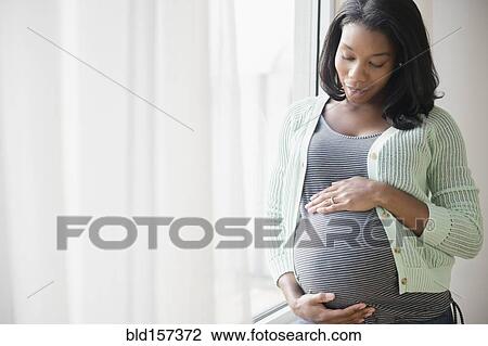Black pregnant woman holding her stomach at window View Large Photo Image Stock Image - Black pregnant woman holding her stomach at window. Fotosearch