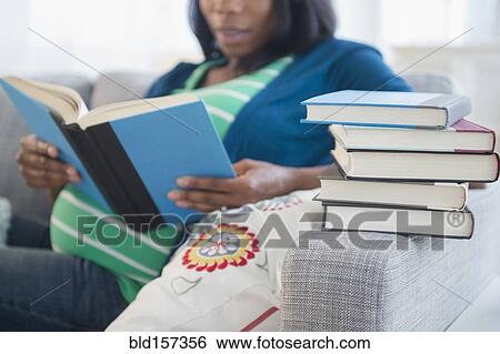 Stock Photograph - Black pregnant woman reading books on sofa. Fotosearch