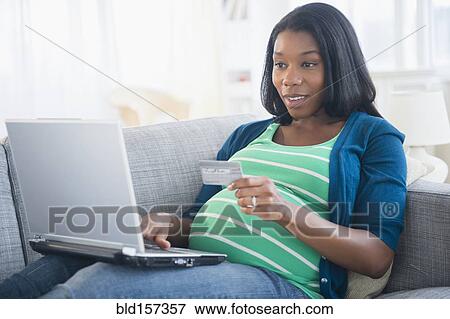 Stock Photo - Black pregnant woman shopping online on sofa. Fotosearch
