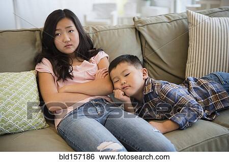 Stock Photograph - Bored Asian brother and sister relaxing on sofa. Fotosearch